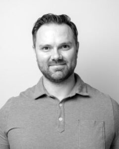 A black-and-white headshot of Brett wearing a collared shirt.