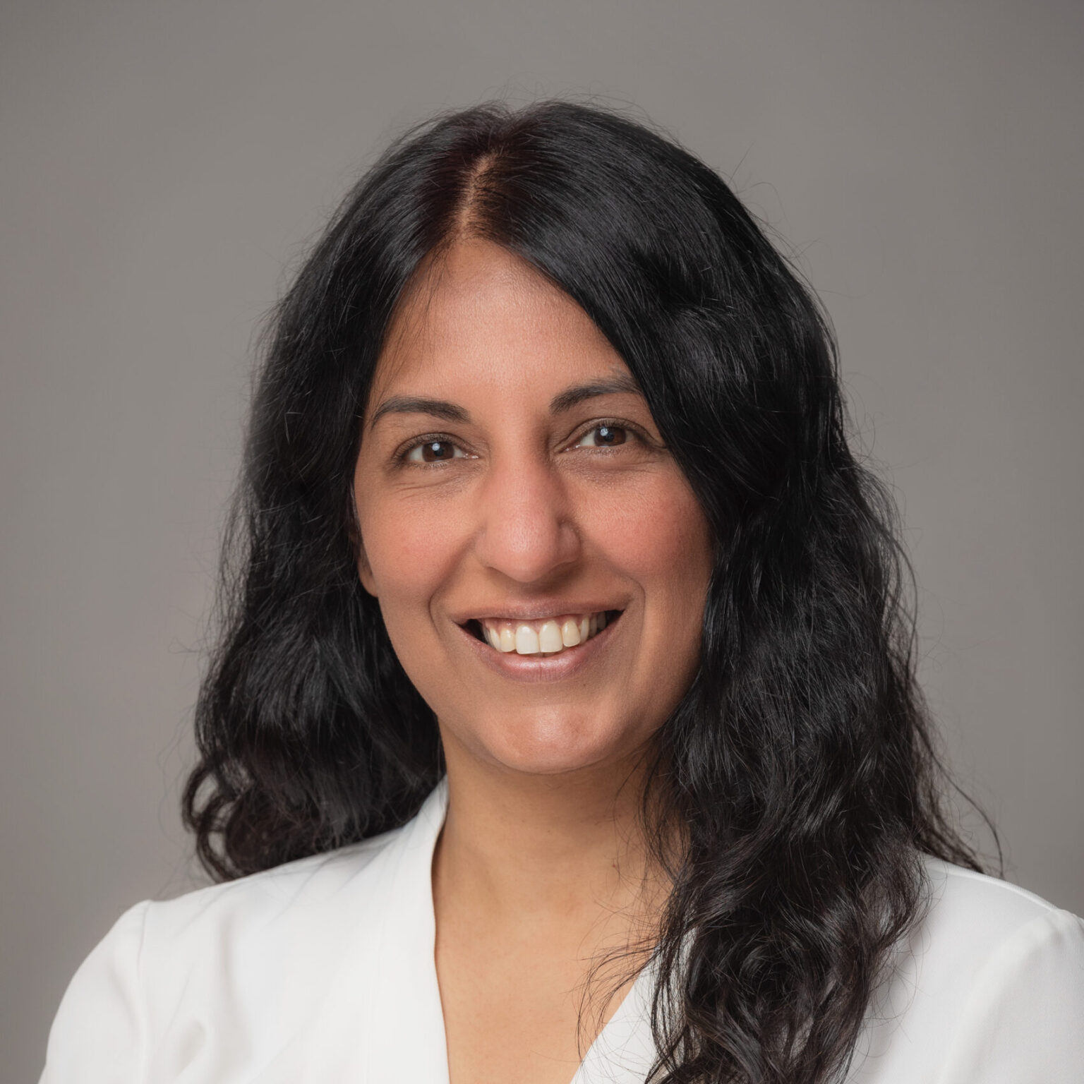 A smiling Anka has long black hair and wears a white blouse.